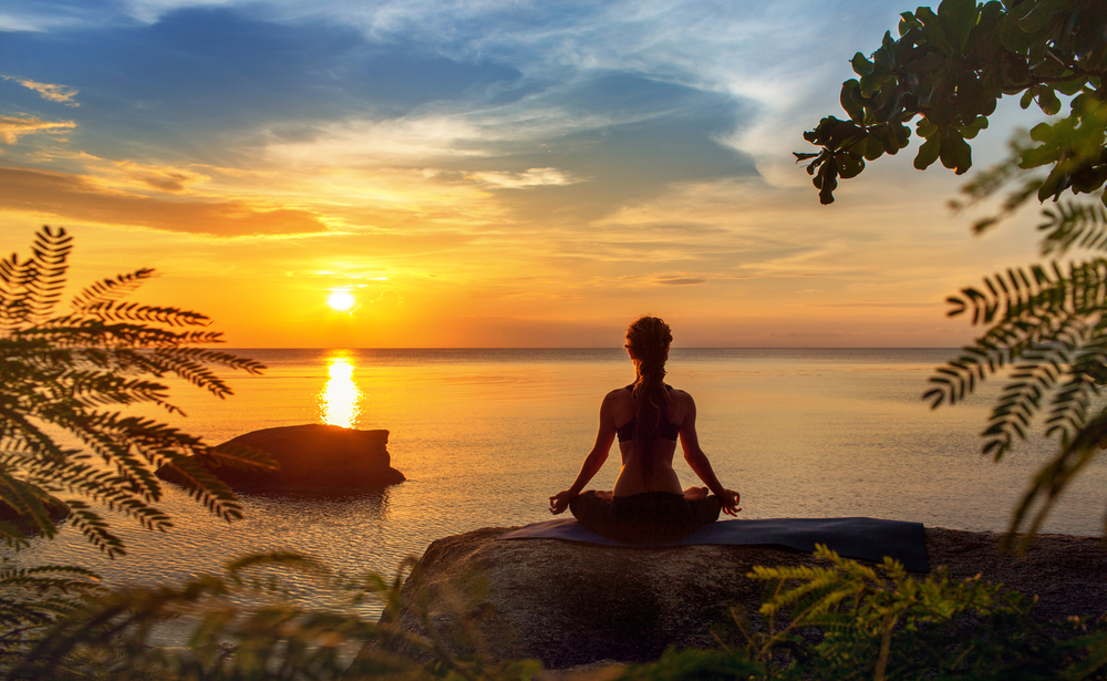 Woman meditating on the beach sunset